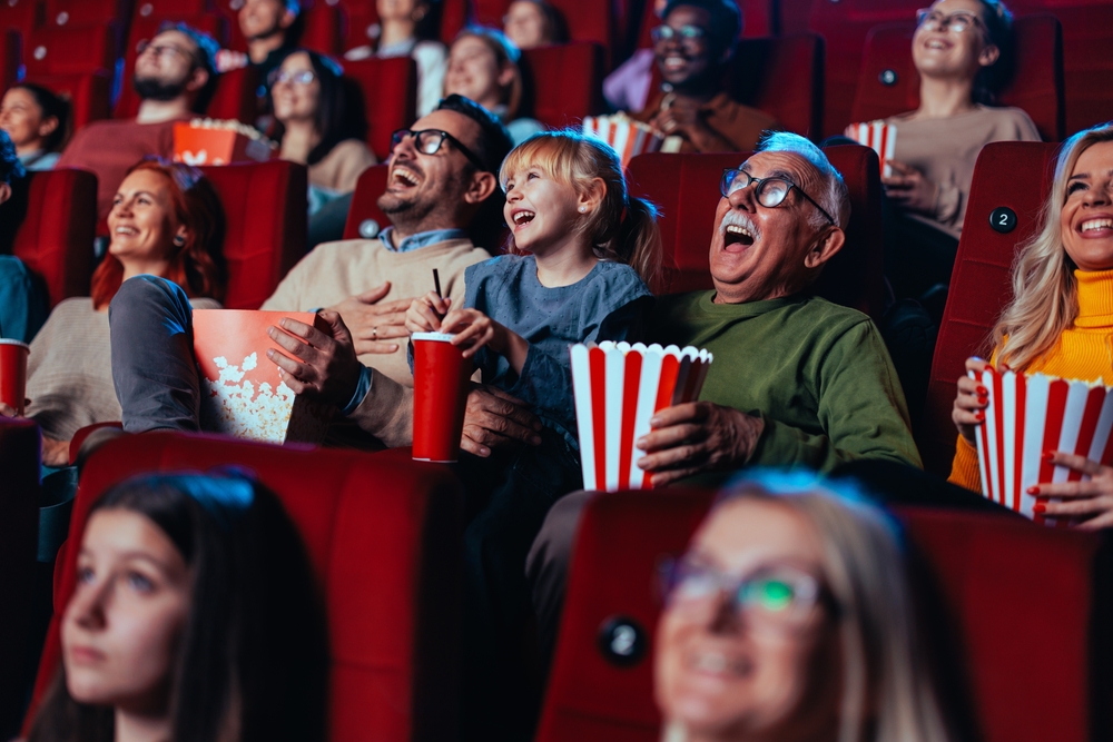 A grandfather and his granddaughter are viewing a summer movie and enjoying themselves and having fun laughing out loud.