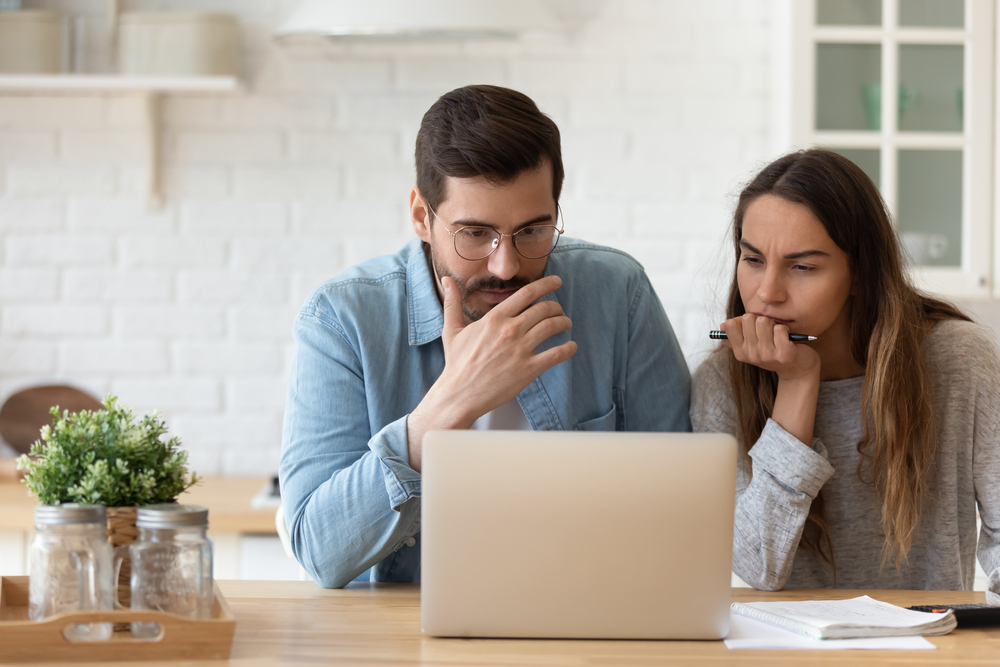 Serious concerned married couple sit indoor looking at laptop read news, receive notification from bank about overspend, financial debt, feel worried, learn new conditions, high rates, taxes concept. So, What Can Geneva Financial Do For You? 
