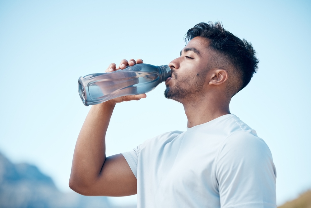 Man, fitness and drinking water in nature exercise, cardio workout or running for sustainability outdoors. Thirsty male person, athlete or runner with drink for hydration, rest or break on mountain
