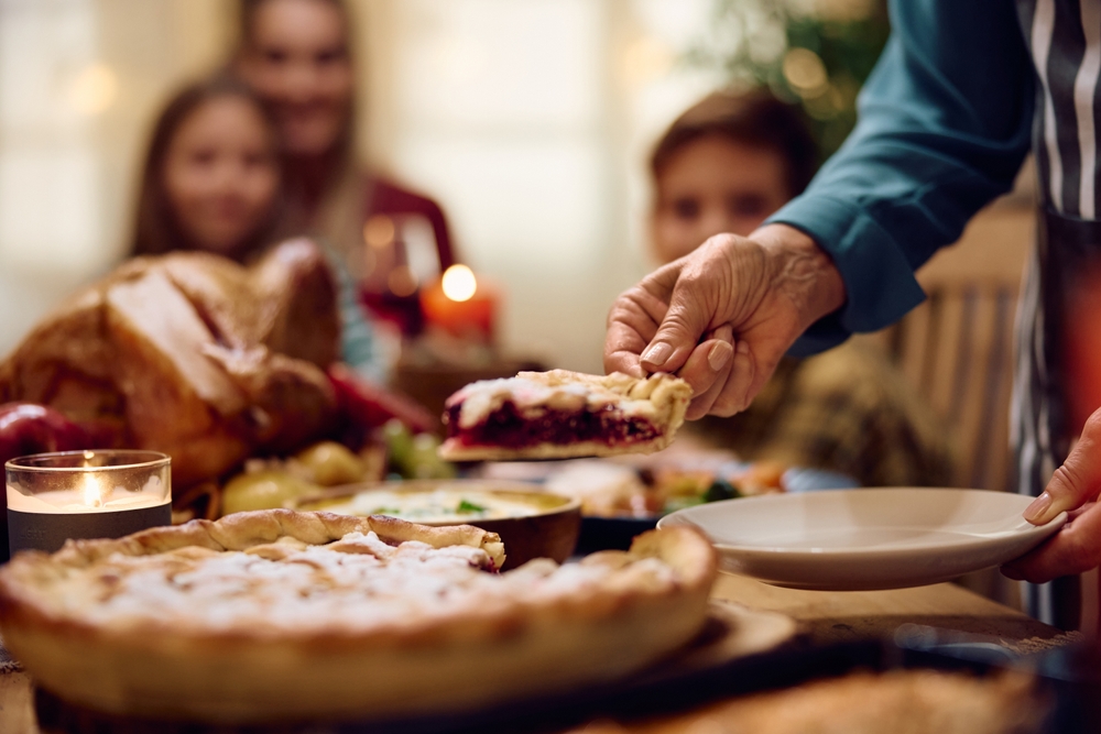 Close up of grandmother serving a slice of sweet pie while having Thanksgiving meal with her family in dining room.