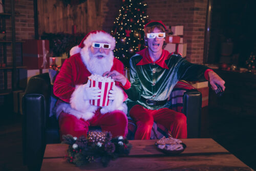 Photo portrait of santa claus and elf eating popcorn using remote watching Christmas movie on sofa in 3d glasses