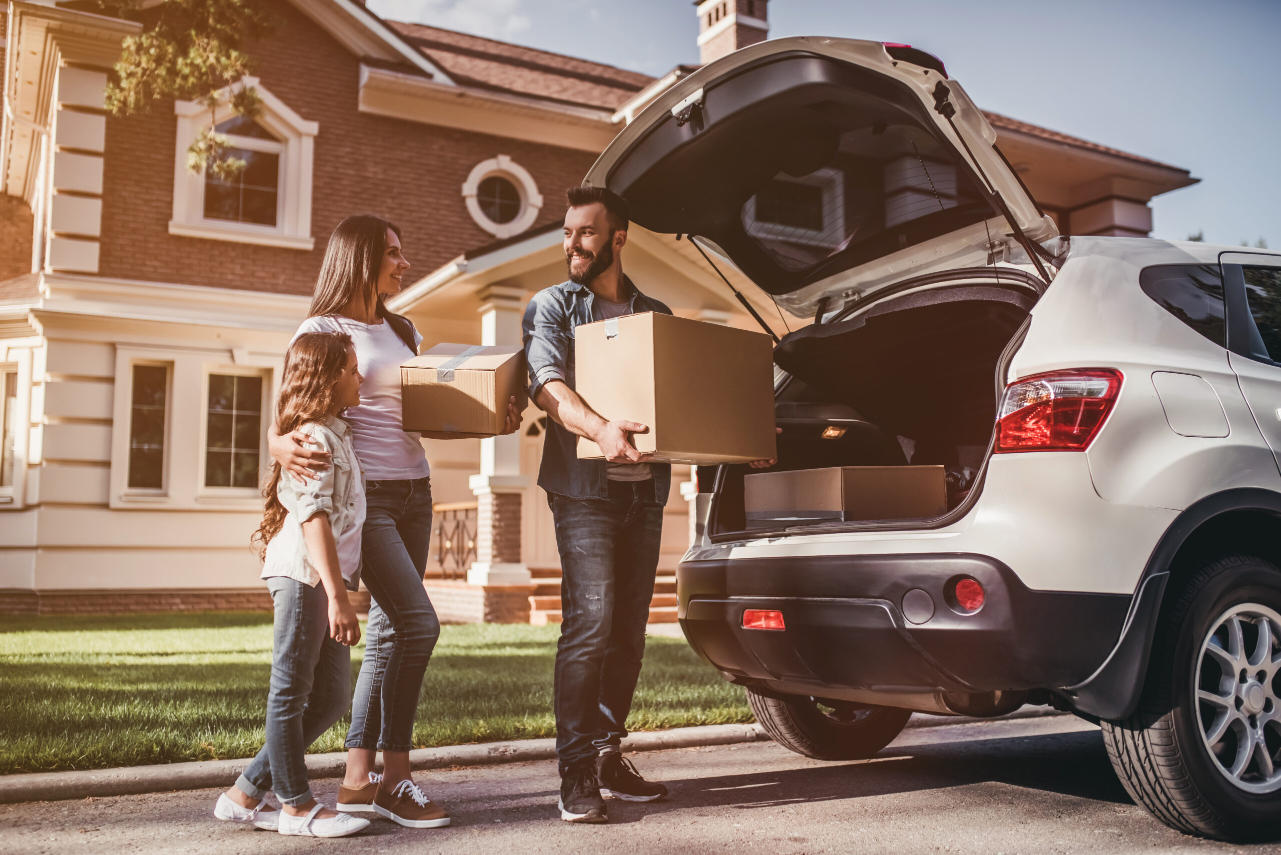 Happy family is standing near car with cardboard boxes. Moving day.