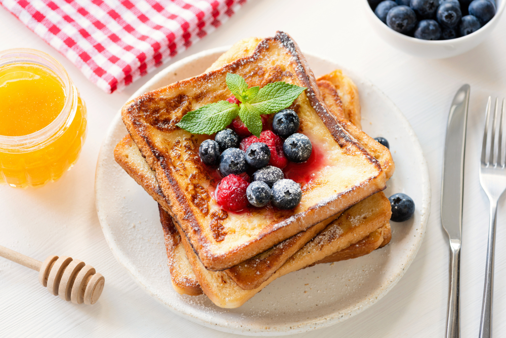 French toast with berries and honey on white plate. 