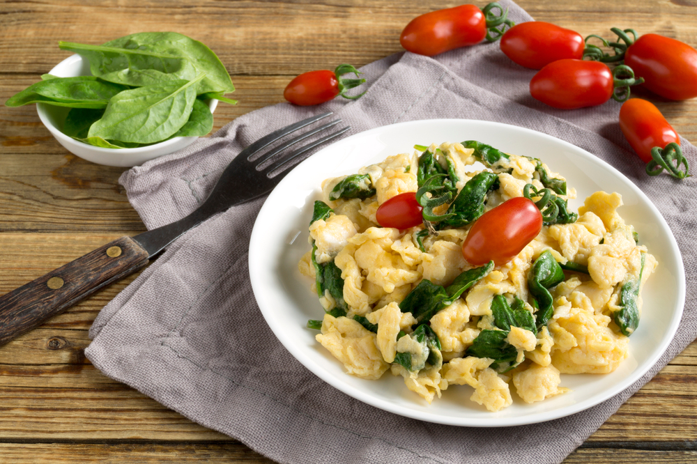 scrambled eggs with spinach and tomatoes on a white plate. on a wooden table
