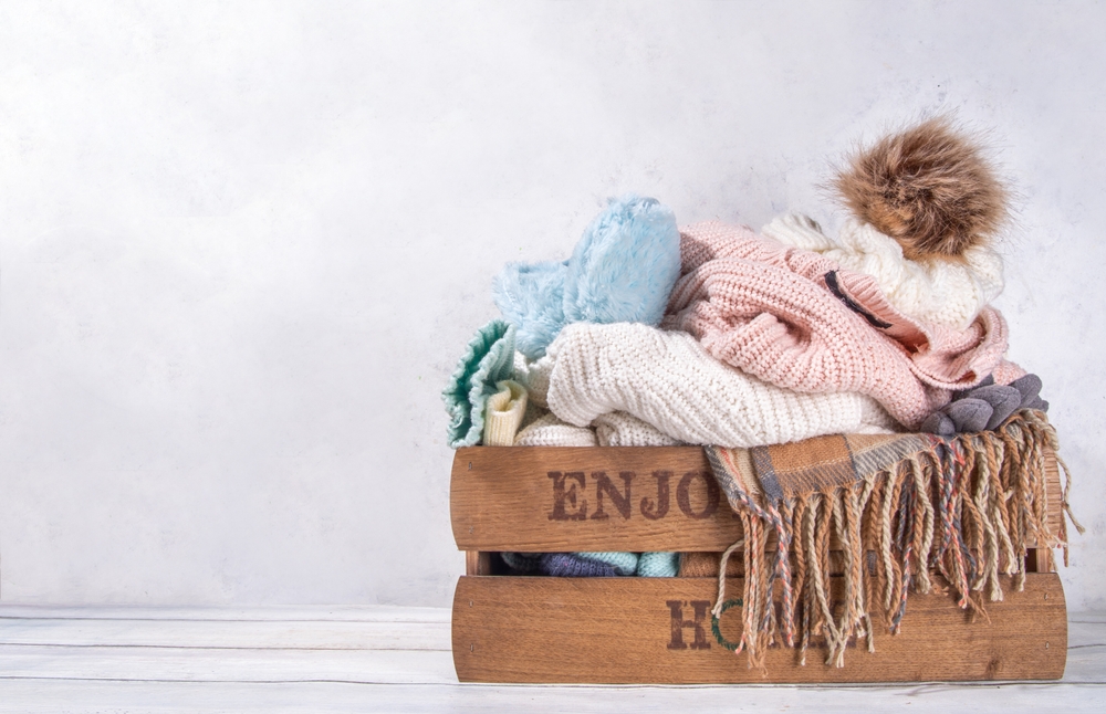 Preparation for fall and winter season, autumn warm cozy clothes, Stack of clean freshly laundered, neatly folded jackets, sweaters, blankets, hats, mittens in wooden box, taken from the mezzanine