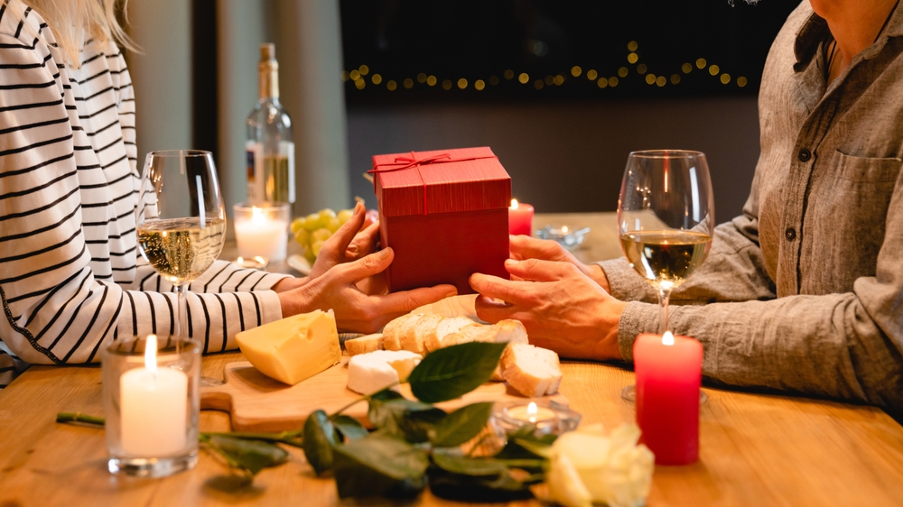 Cropped close up photo of lovers` hands giving each other presents for anniversary or St. Valentines Day during romantic dinner. Gift receiving - love language