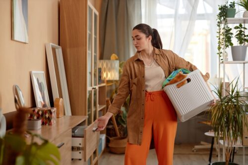 Side view portrait of young woman putting away clean clothes on laundry day, copy space